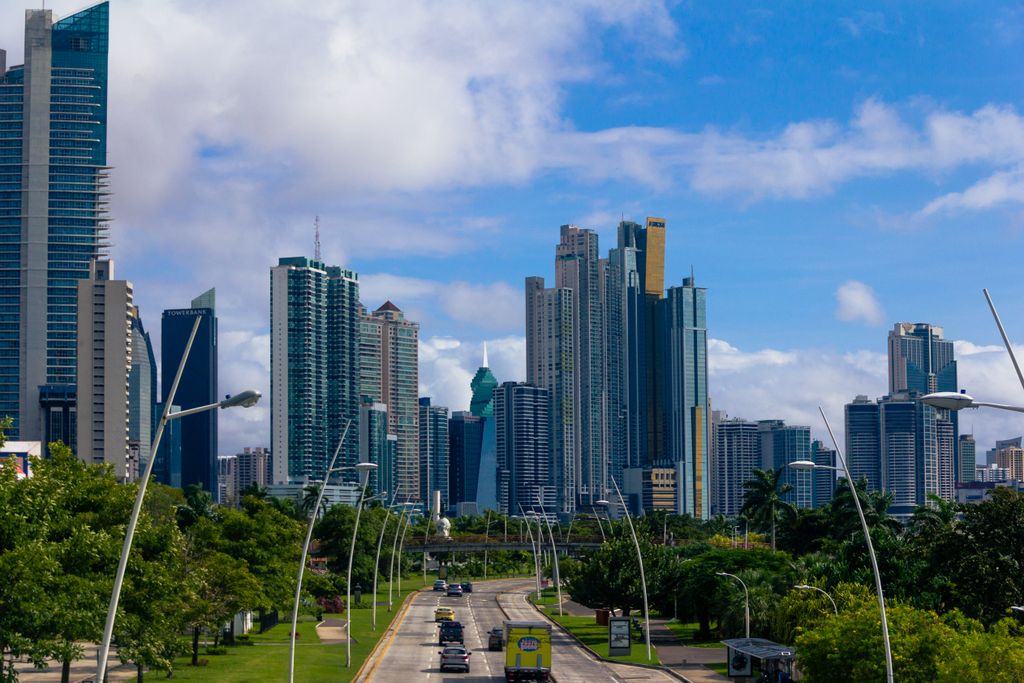 Modern skyline of Panama City with clear blue skies and lush greenery alongside the roadway.